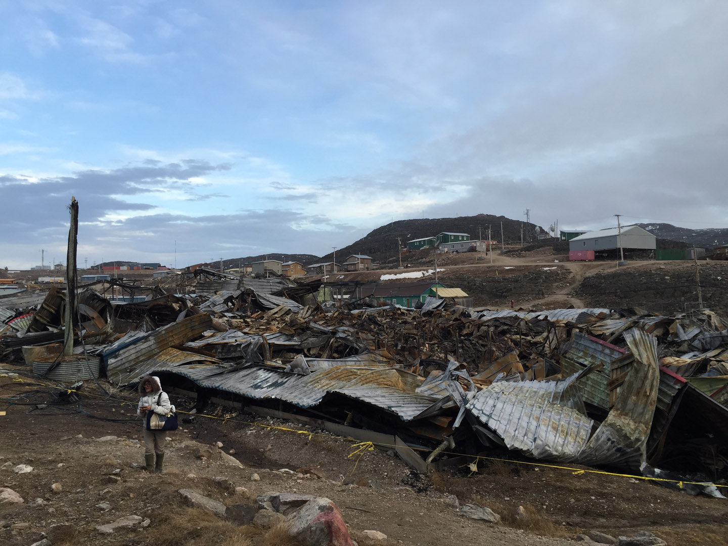 Shuvinai standing in front of Peter Pitseolak high school, which was burnt down by local teens on Sept. 6, '15. The idea of school is a complicated place when people from your family have been historically abused or forced to go there. Residents also lost the day care and community centre in the fire. 